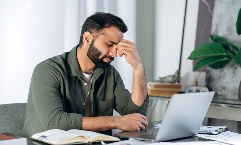 An employee who’s frustrated and sitting in front of their computer with hands on the head