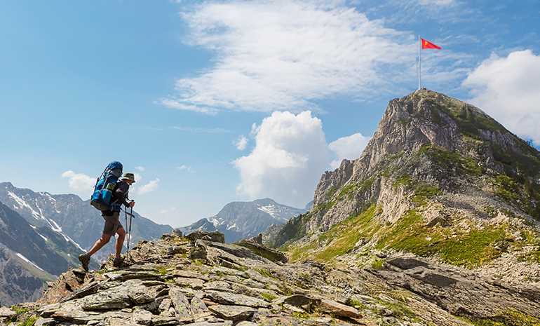 An individual is climbing a mountain that has a flag on top of it that denotes their goal