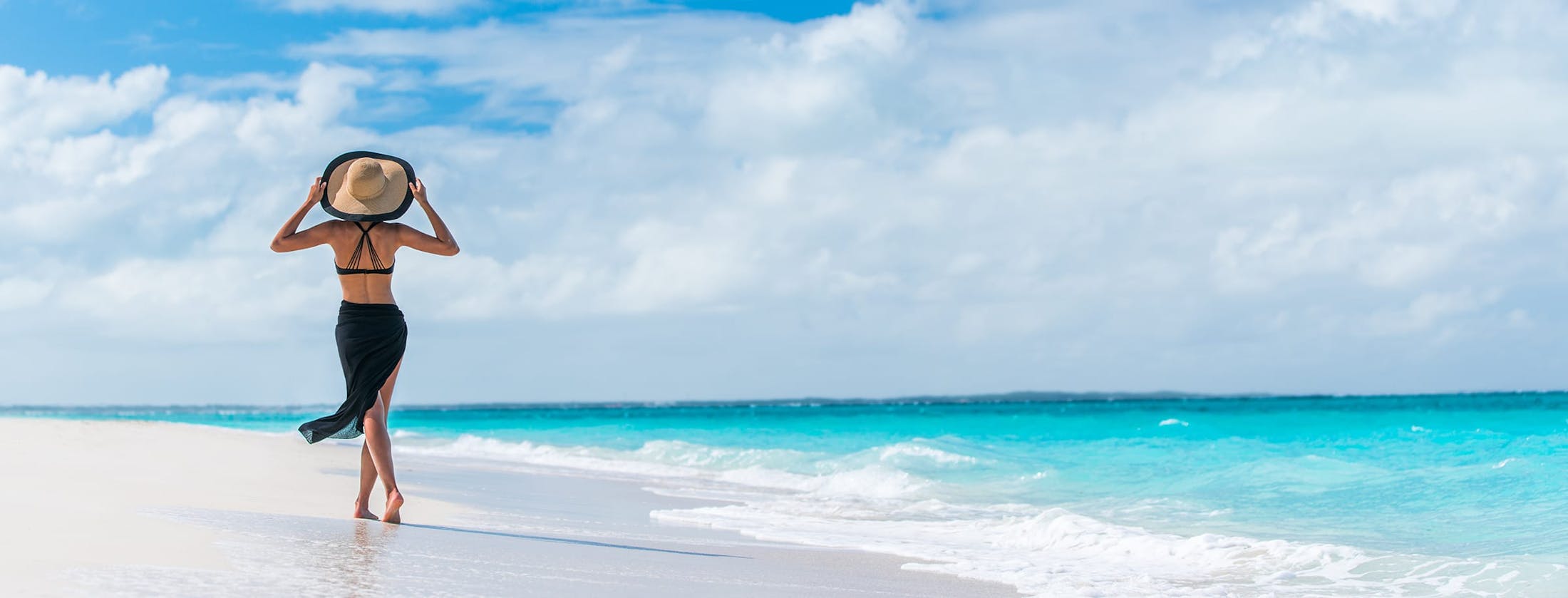 Woman walking down the beach holding her hat