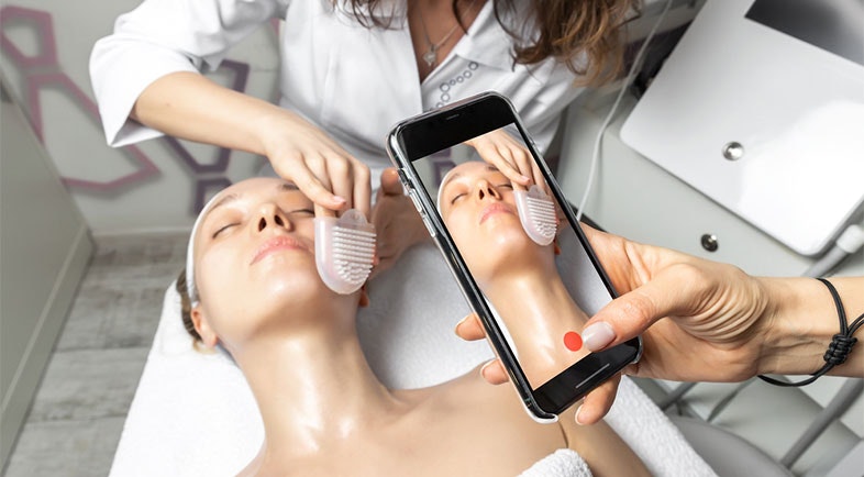 A hand holding smartphone making online live video stream of cosmetician doctor facial care procedure 