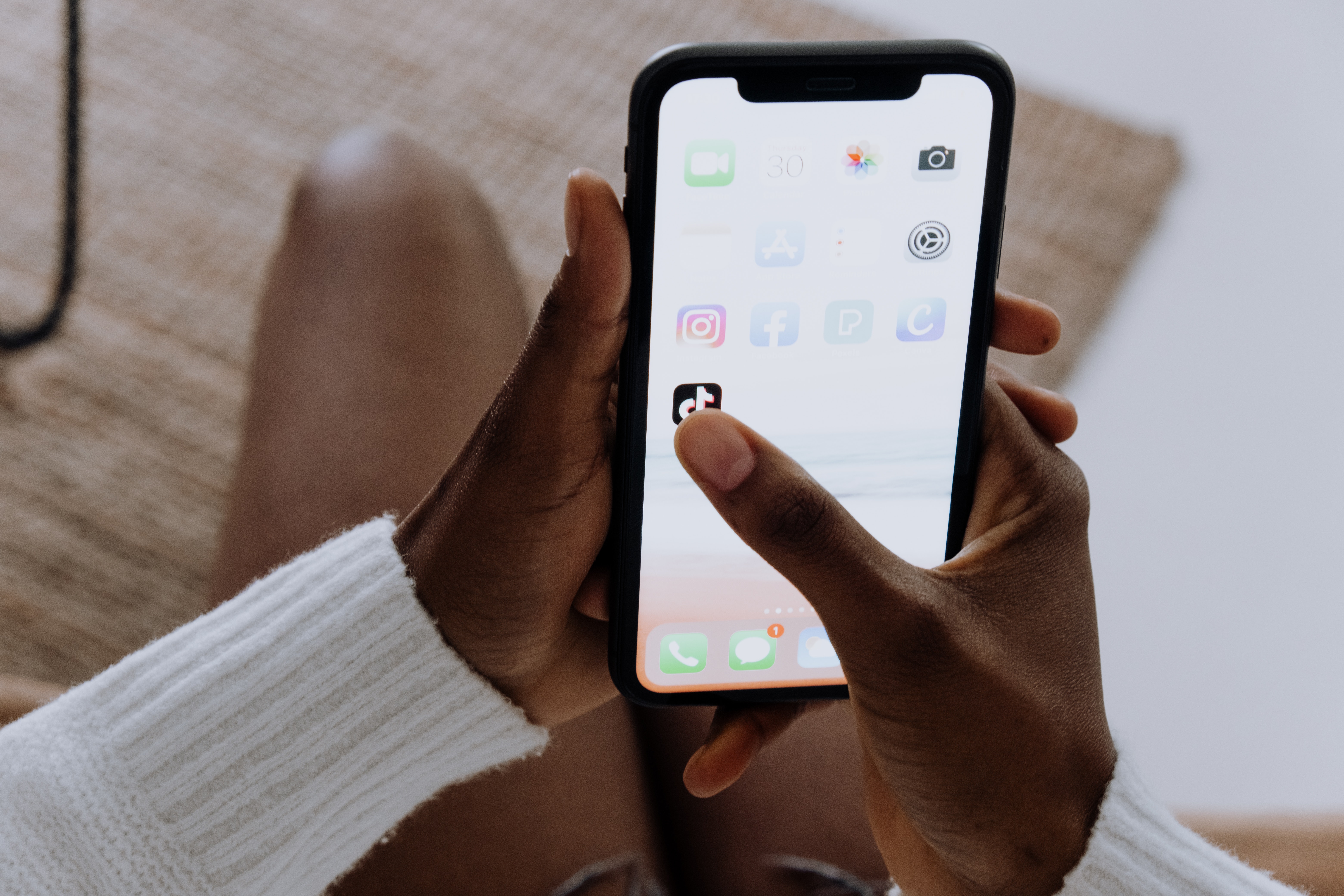 Person holding black iPhone with thumb hovering over TikTok app icon