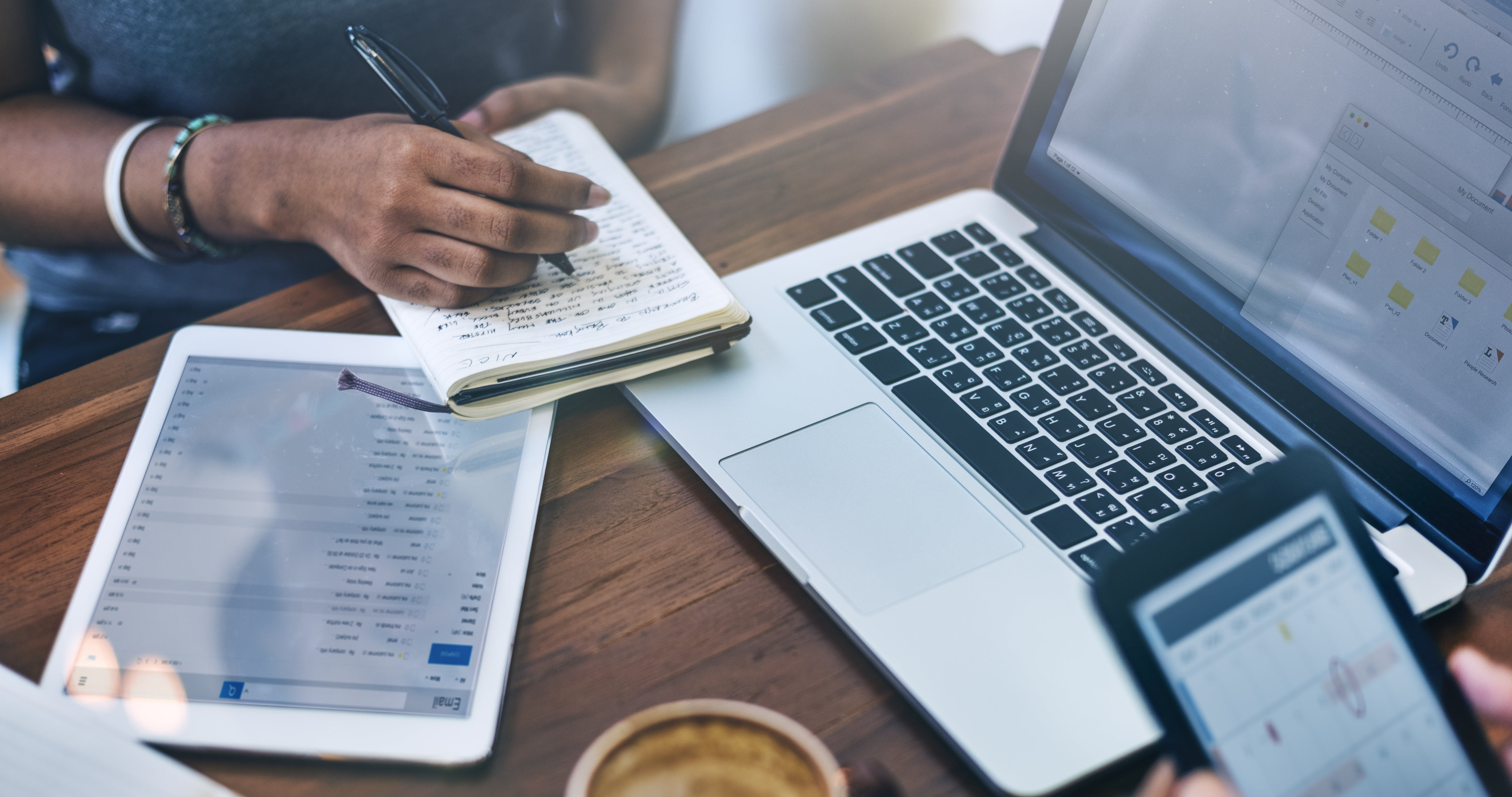 Woman writing in a notebook on desk next to laptop