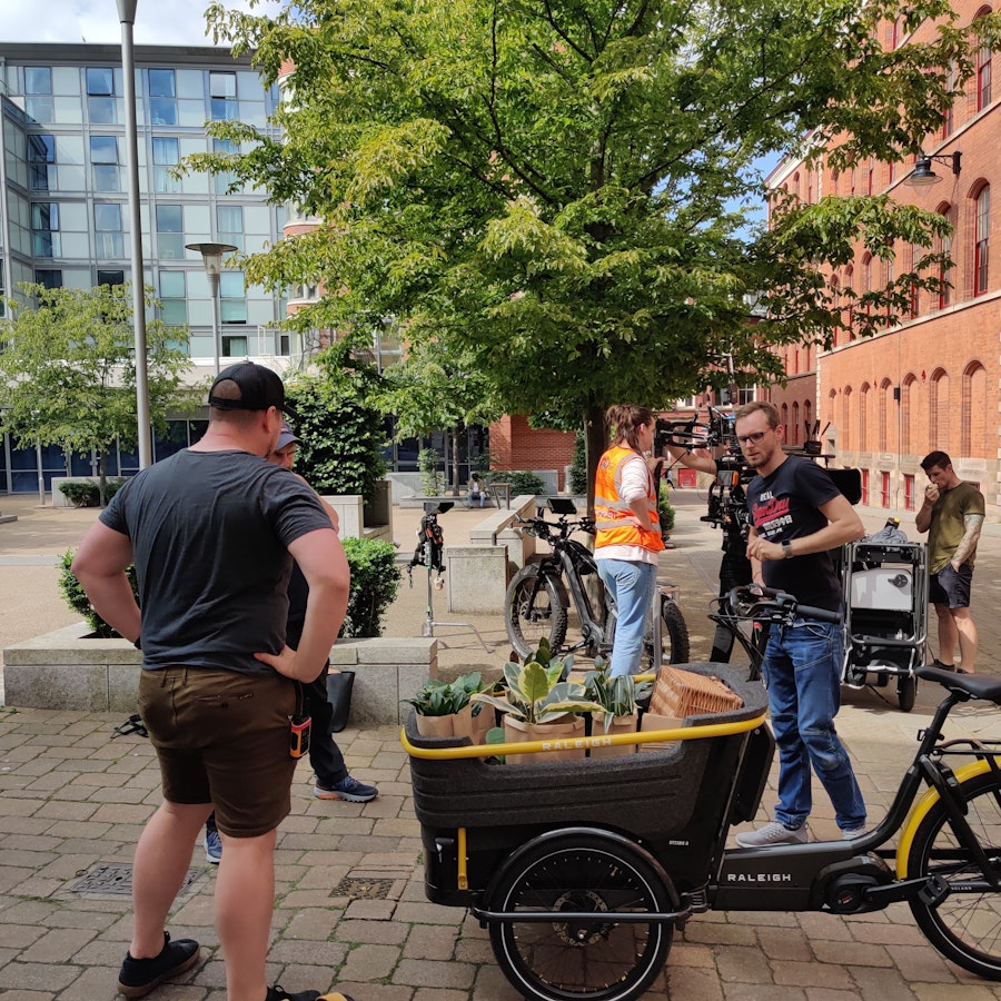 A Raleigh Stride Cargo bike is in the foreground with plants in the basket. Crew are in the background. A BTS shot from the Raleigh Bike Stride Cargo Bike Shoot in Nottingham