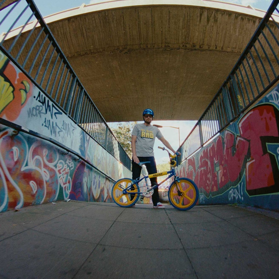 A man standing behind a BMX Burner Bike surrounded by graffiti art