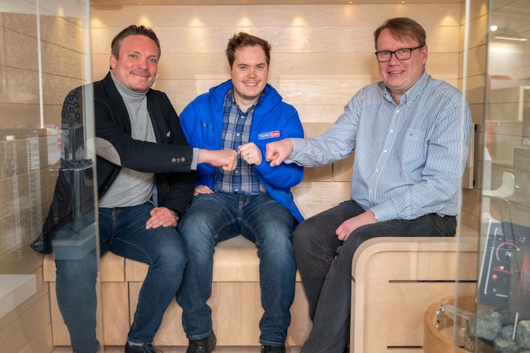 Three men sitting on sauna benches while bumping fists together