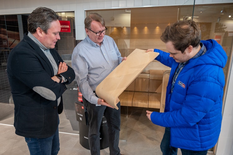 Man showing a part of sauna bench to two other men