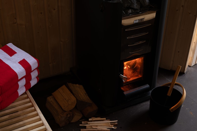 A sauna stove, with a fire inside. A bench with towels next to it.