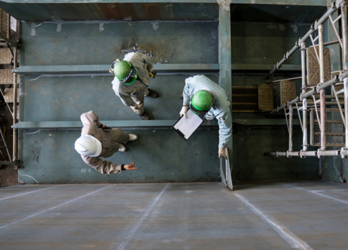 A photo with a view from directly above of three men talking in a large shipbuilding factory