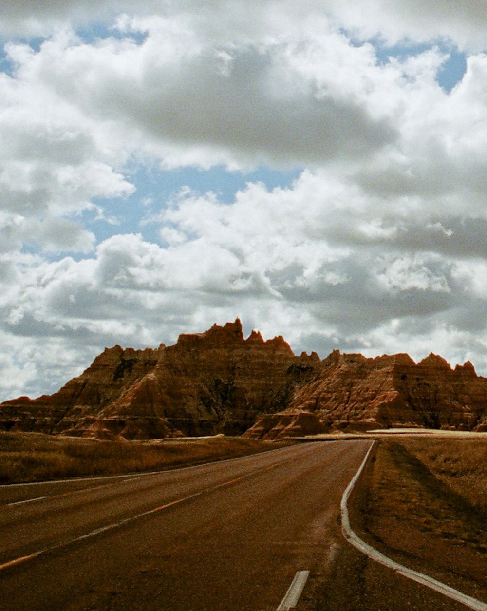 A photo of a desert road under clouds leading to a mountain