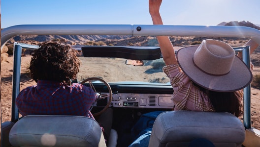 A photo of a young man and woman driving in a vintage car on a desert road