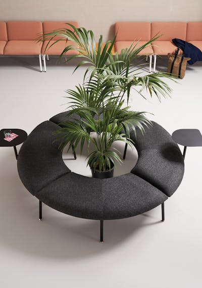 Mega armchair with built-in coffee tables arranged around a plant