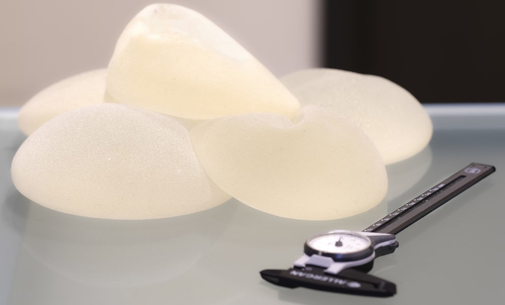 Silicone breast implants stacked on a table next to a measuring device.