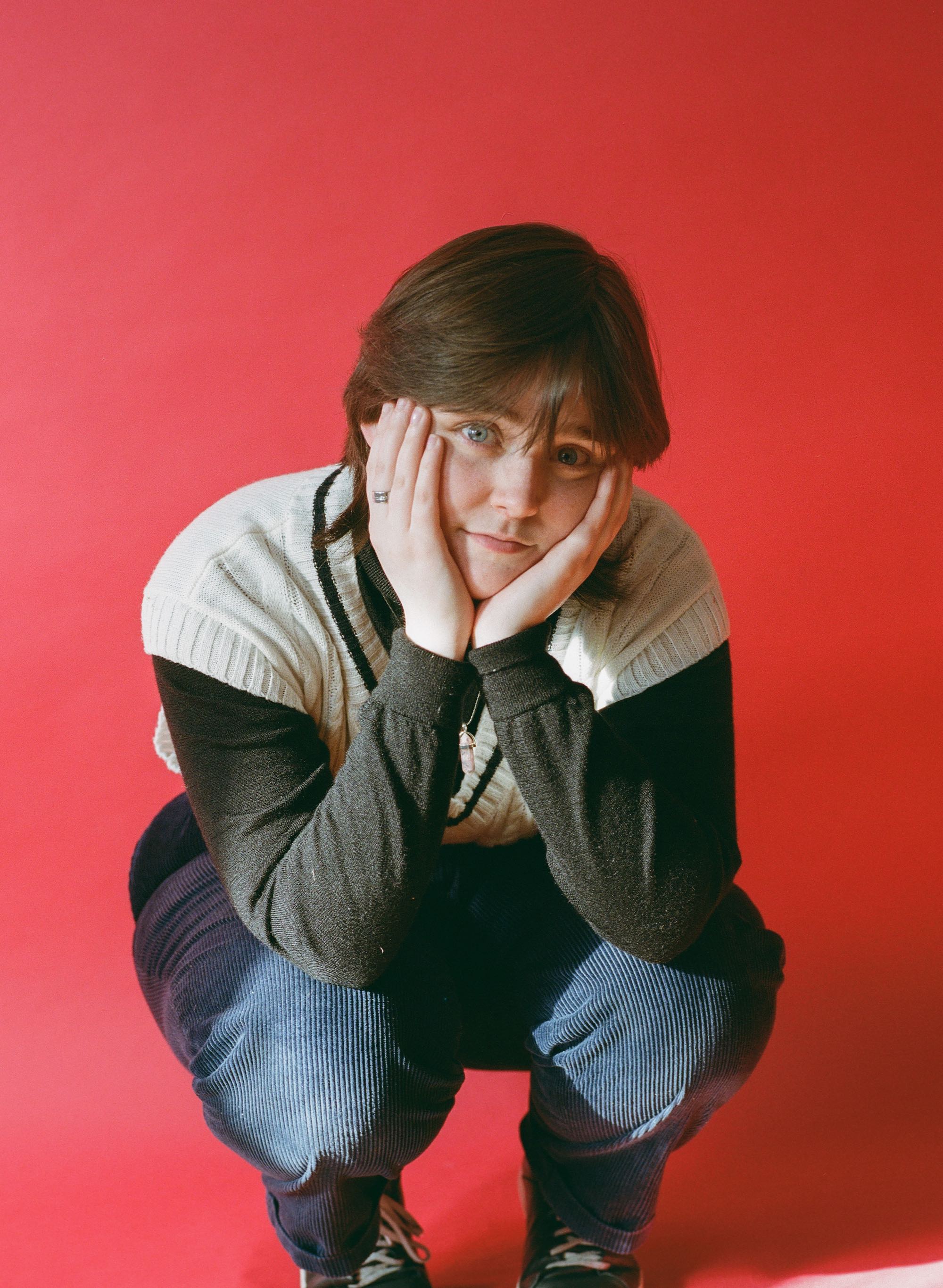 Sammy Copley crouching with faces in hands in front of pink background