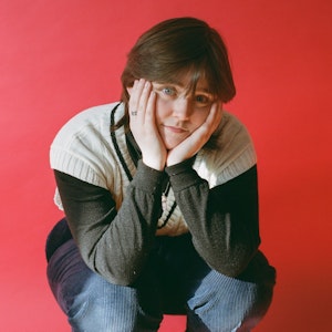 Sammy Copley crouching with faces in hands in front of pink background