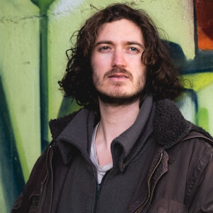 Ezra stands against graffiti under bridge