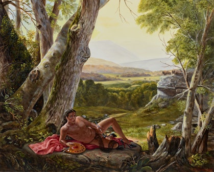 A person lies on their side under a large tree, with views of fields and hills in the background.