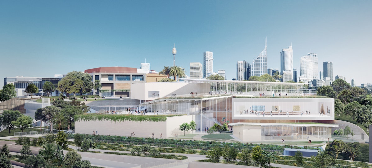 A large white building consisting of several differently shaped tiers in a landscaped setting with tall city buildings in the distance