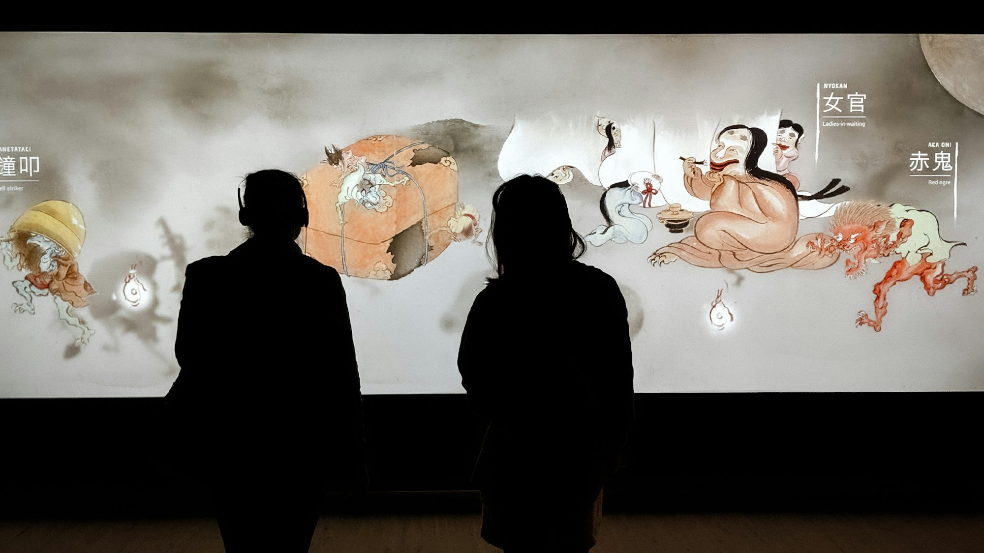 Visitors enjoying the Japan Supernatural interactive touch wall featuring characters from Hiroharu Itaya Night procession of one hundred demons circa 1820 (detail)