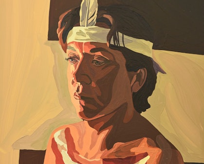 An Aboriginal woman with short dark hair is turned slightly to the right. Her face and chest are painted and she is wearing a headband into which is tucked a single feather at the front.