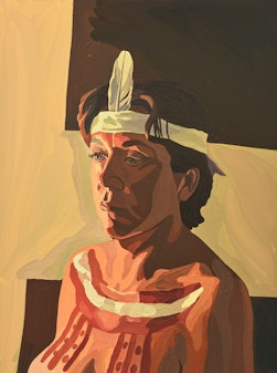 An Aboriginal woman with short dark hair is turned slightly to the right. Her face and chest are painted and she is wearing a headband into which is tucked a single feather at the front.