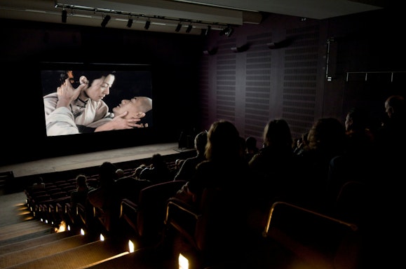 People sit in a darkened cinema watching two people on a large screen