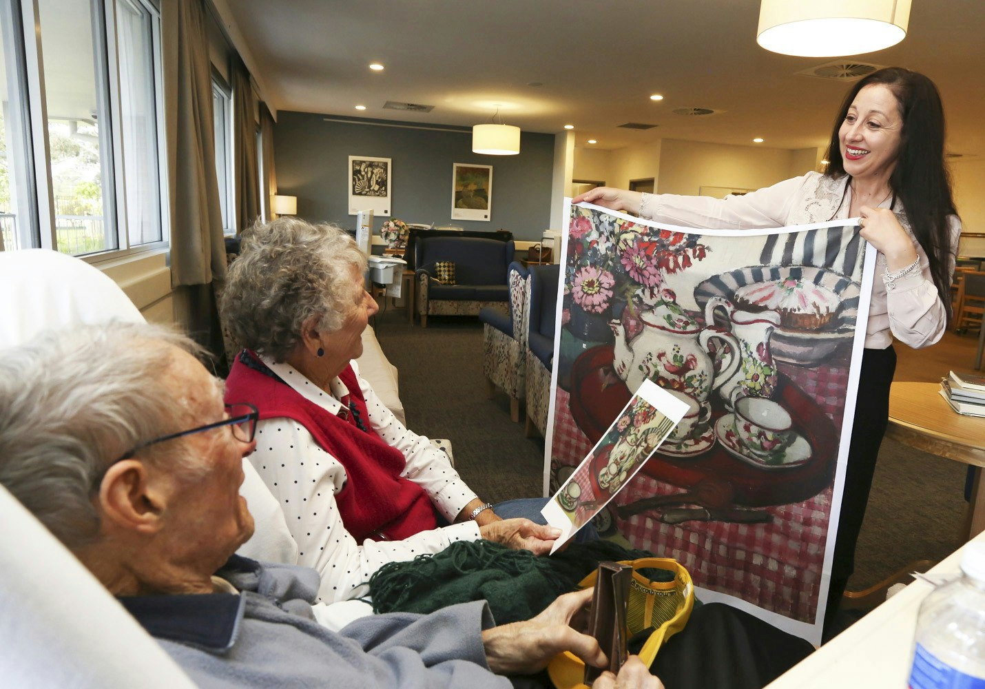 left to right: Murrumburrah-Harden Health Service resident Woodley Smith with his wife Dorothy Smith and Danielle Gullotta (Art Gallery of NSW) at Murrumburrah-Harden Health Service. Photo: Brett Naseby.  Artwork: Margaret Preston, Thea Proctor’s tea party 1924. © Margaret Rose Preston/Copyright Agency, Sydney.