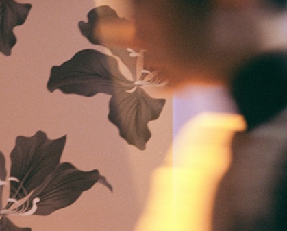A figure blurred by movement in front of wallpaper of orchids, the national emblem of Hong Kong.
