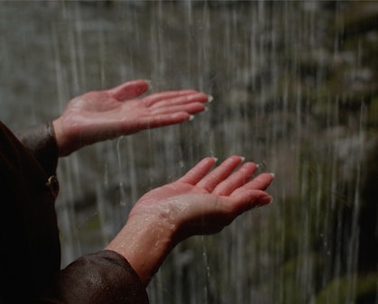 Video still of two hands with palms facing upwards as water falls on them.