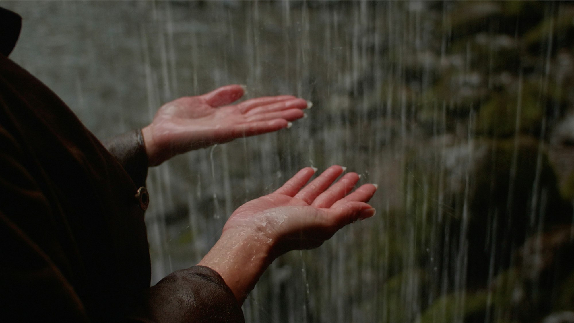 Video still of two hands with palms facing upwards as water falls on them.