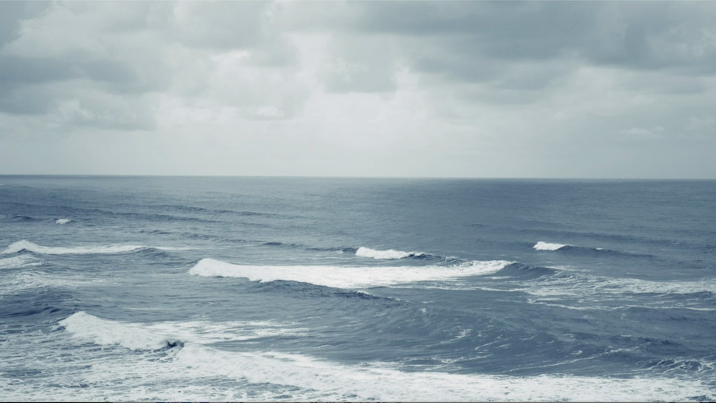 Video still of waves rolling beneath an overcast sky.