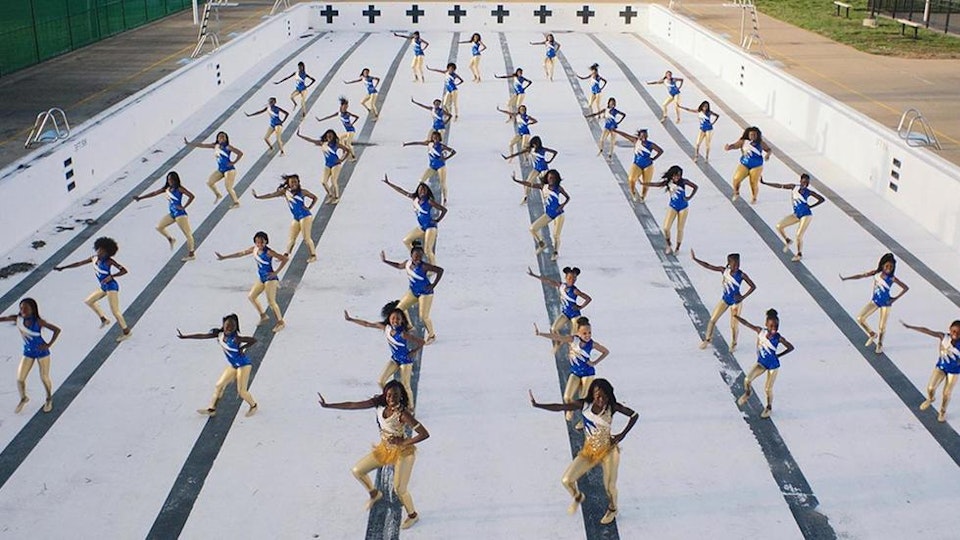 Video still of 6 rows of people performing synchronised choreography in an empty swimming pool.