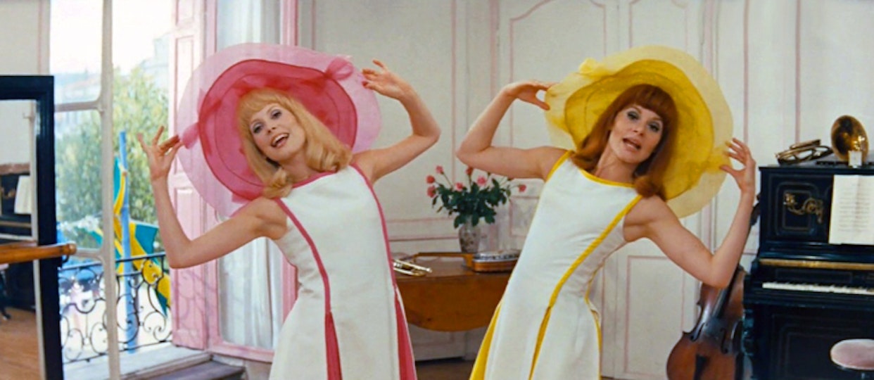 Video still of two women in matching pink, yellow and white outfits in a room.