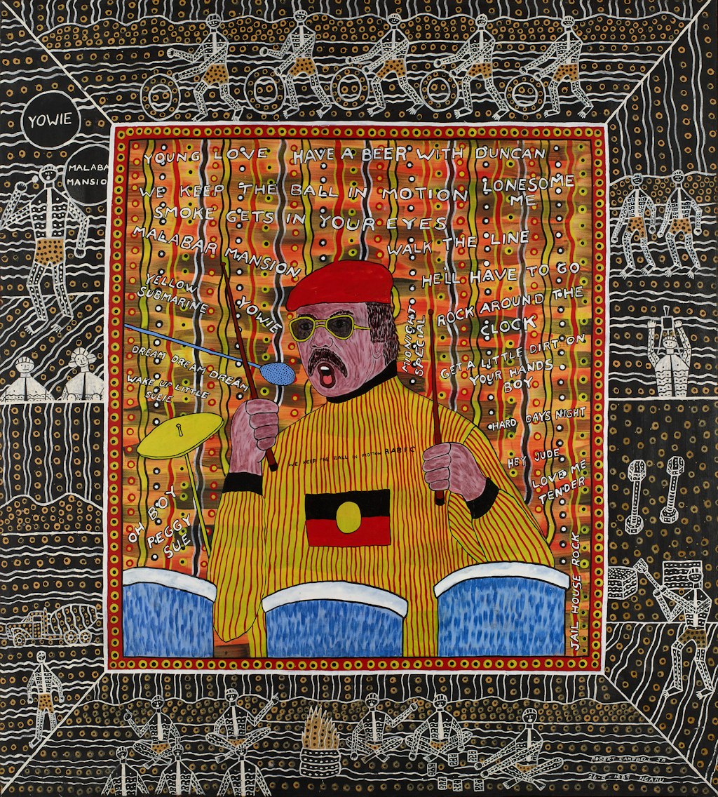 A man at a drumkit with his drumsticks raised. He has brown hair and a moustache, and is wearing a beret, sunglasses and a long-sleeved top with the Aboriginal flag on the chest. The titles of songs are written on the patterned background. An outer boarder depicts multiple figures on a background of different patterning.