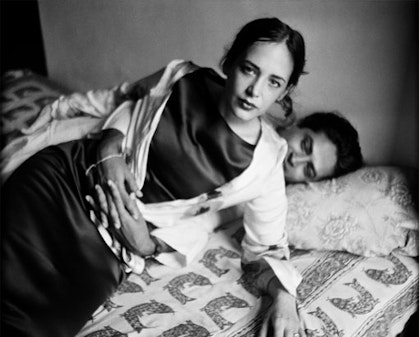 Two people on a bed, with one person propped up on their arm and the other lying behind them