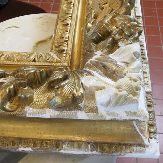 The right lower corner of the frame during treatment, showing replaced missing parts of ornaments in the gesso/compo stage.