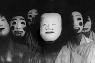 Black and white film still of 7 people wearing masks looking in the direction of the camera.