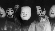 Black and white film still of 7 people wearing masks looking in the direction of the camera.