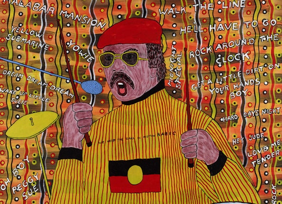 A man at a drumkit with his drumsticks raised. He has brown hair and a moustache, and is wearing a beret, sunglasses and a long-sleeved top with the Aboriginal flag on the chest. The titles of songs are written on the patterned background.