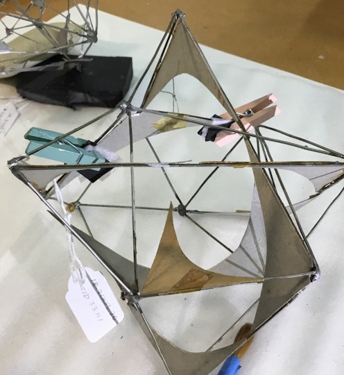 Two pegs are clipped to a silver-coloured sculpture of interconnected open geometric shapes