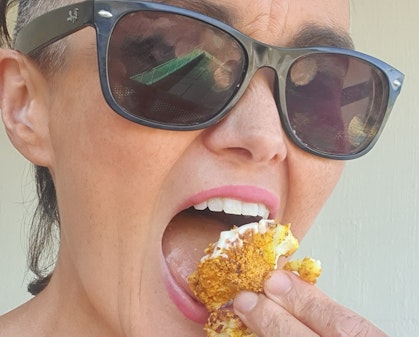 A woman in sunglasses eating crumbed cauliflower.