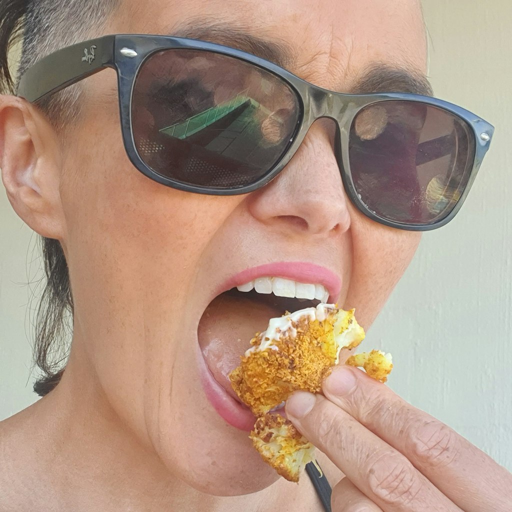 A woman in sunglasses eating crumbed cauliflower.
