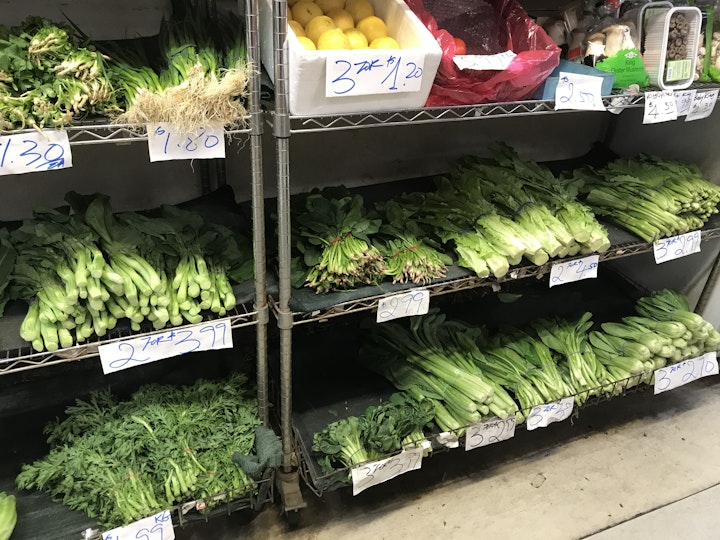 Shelves in an Asian grocery stocked with various green vegetables.