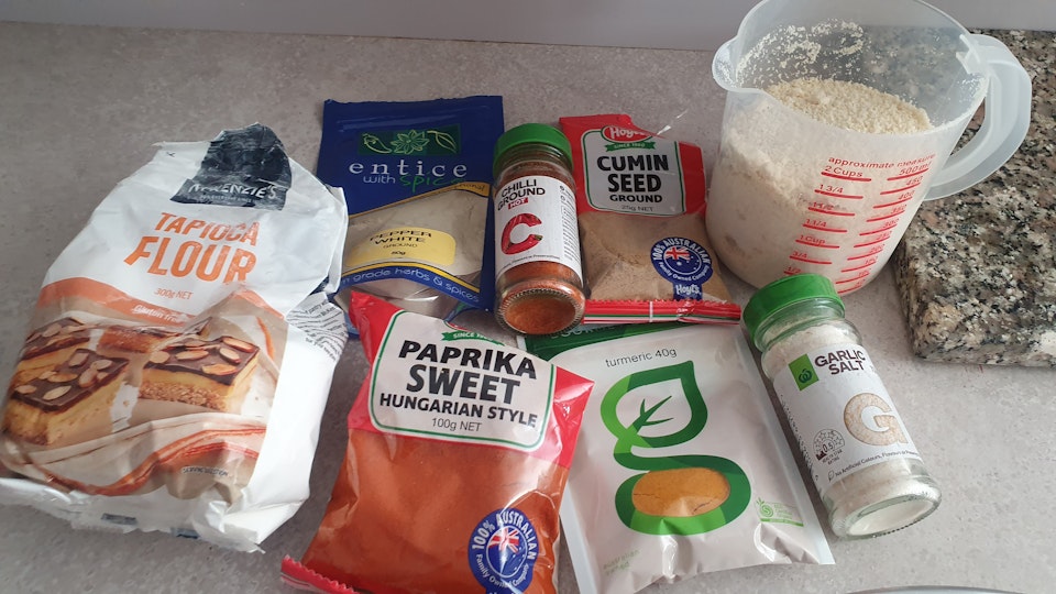 Packets of tapioca flour, sweet paprika, cumin seed, turmeric. Jars of chilli powder and garlic salt. Measuring cup containing flour.