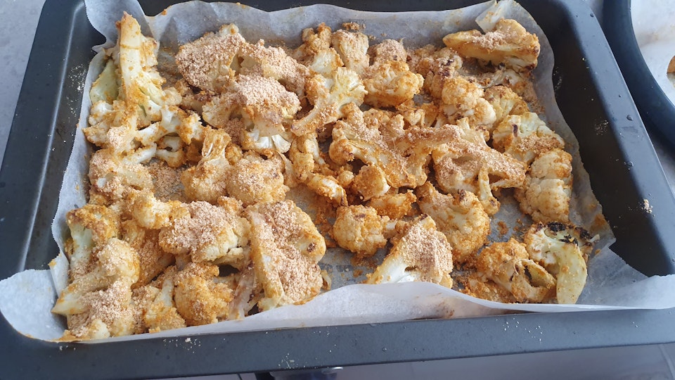 A paper-lined baking tray containing crumbed cauliflower pieces.