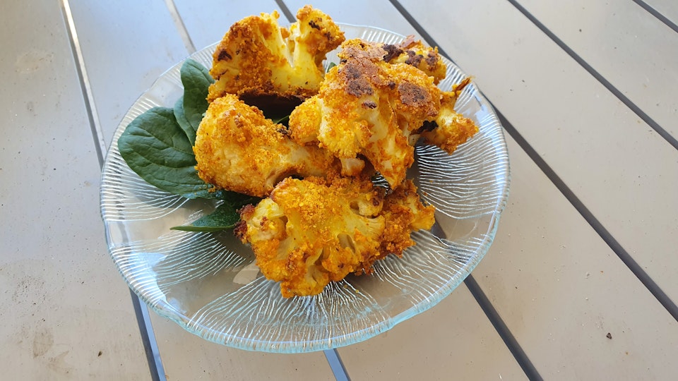 Fried crumbed cauliflower pieces on top of green leaves on a glass plate.