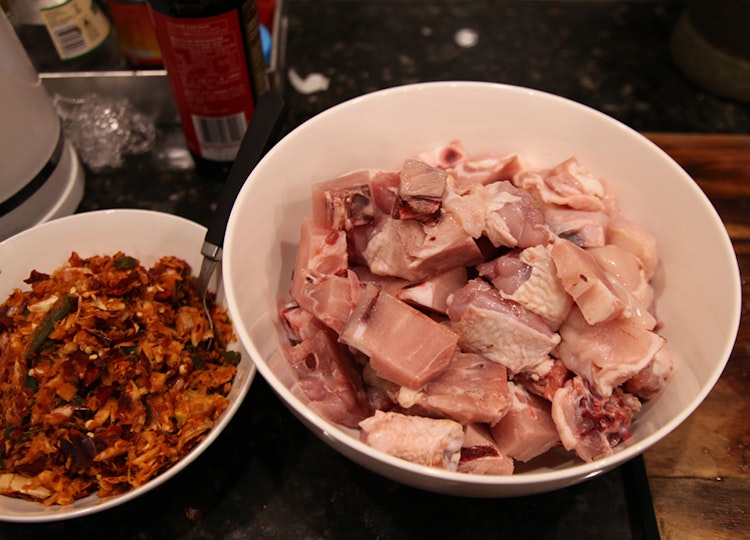 A large bowl of raw chicken pieces and a smaller bowl of mixed ingredients.