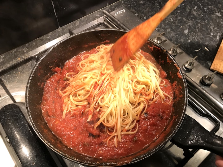 Linguine is stirred, with a wooden spoon, into tomato-based sauce in a frypan.