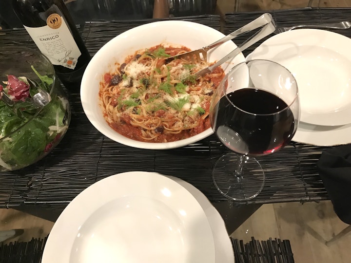 A table set with a bowl of pasta, a bowl of salad, a wine bottle, a glass of red wine and two shallow bowls.