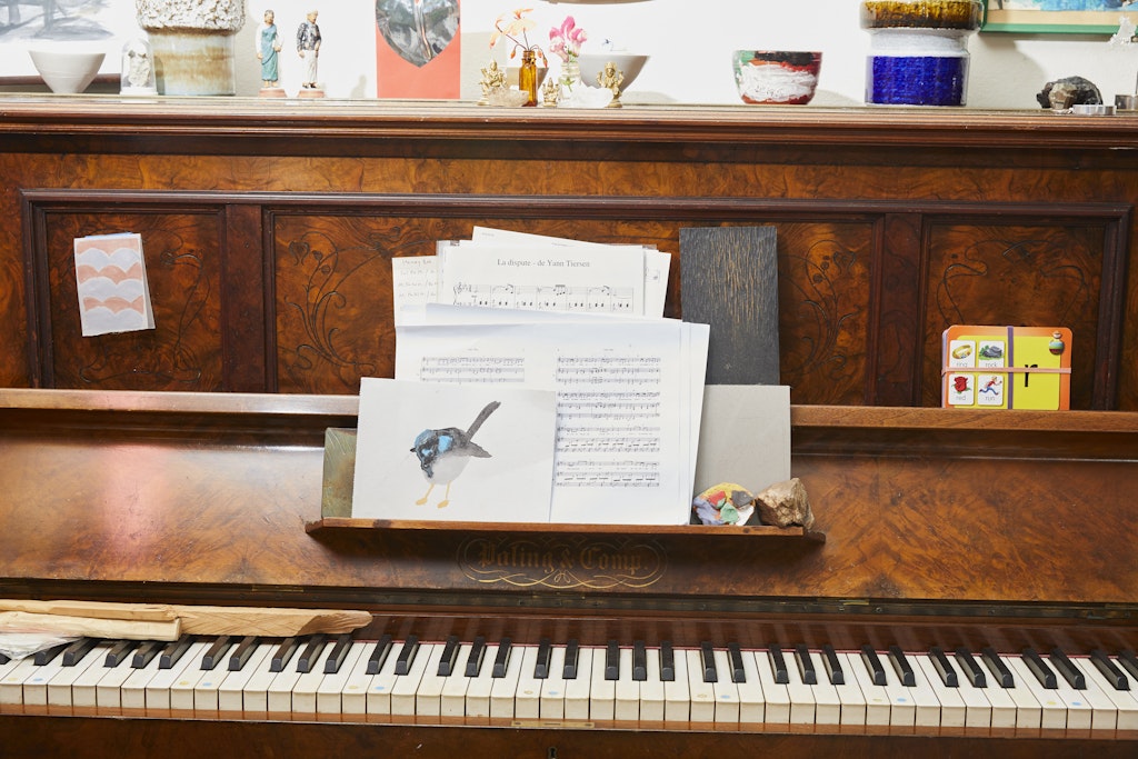 A piano with lots of objects on top of the instrument and on its music holder.