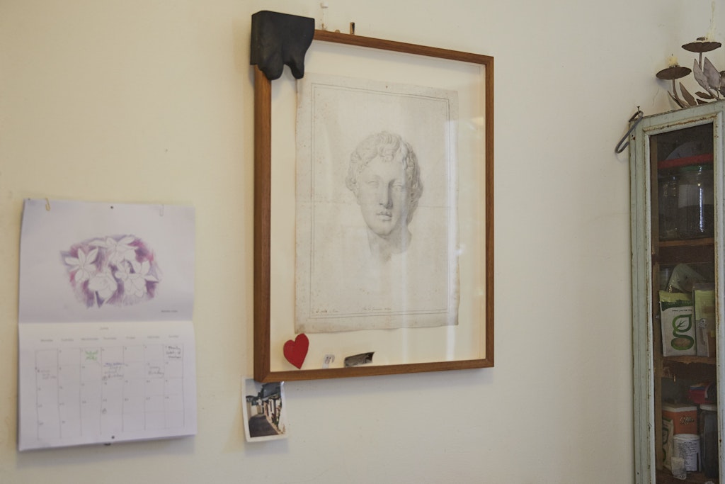 A framed drawing of the head of a classical sculpture with various items tucked into the frame. Next to it is an open calendar.